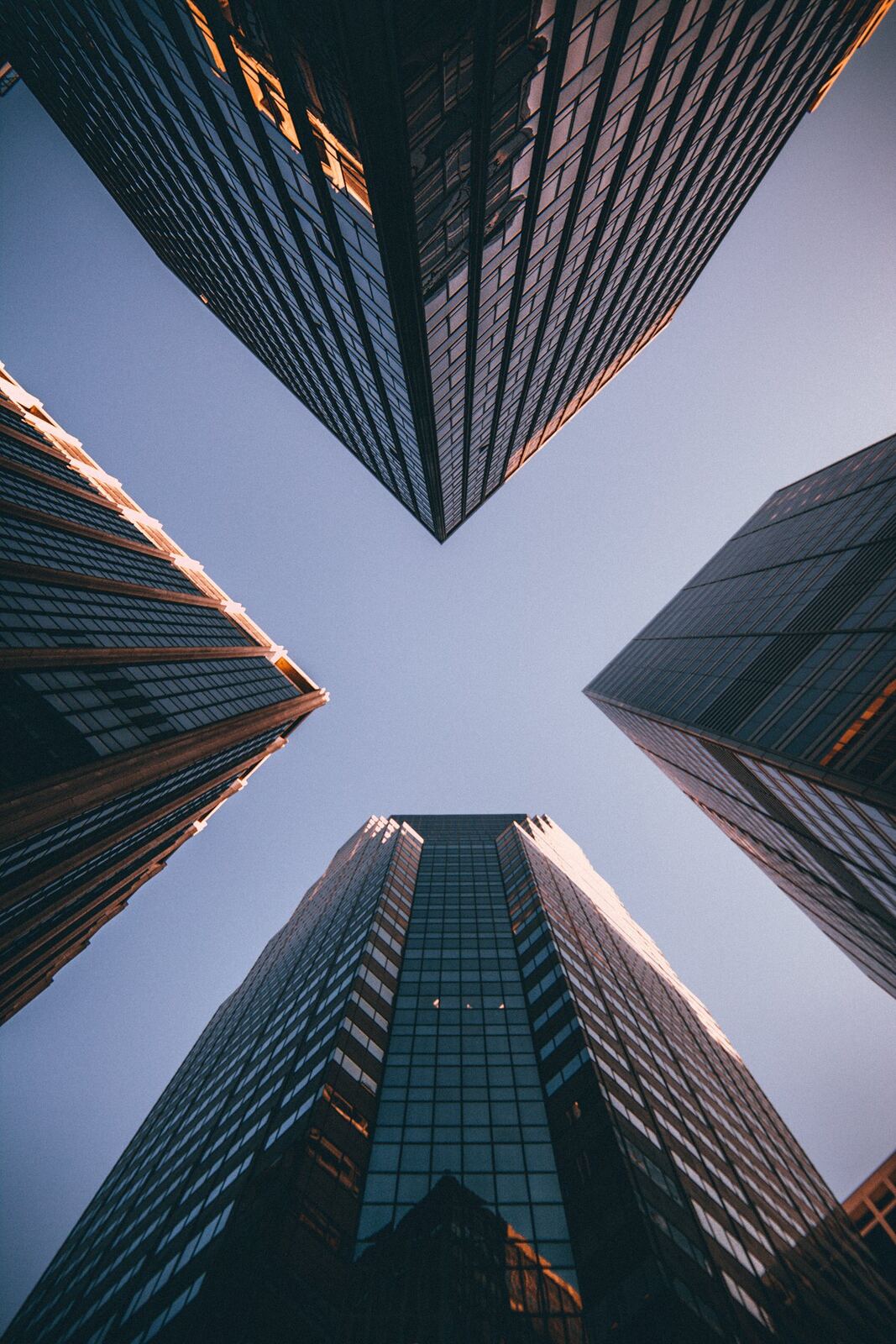 Glass office towers photographed from street level, their edges lit gold against a deep blue sky